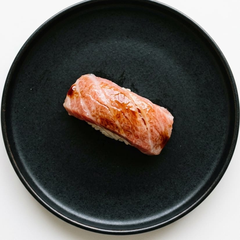 A single piece of otoro nigiri on a black plate, brushed with nikiri